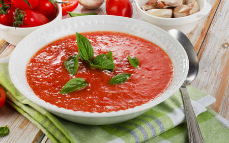 Fresh tomato soup in a white bowl on a wooden tableの写真素材