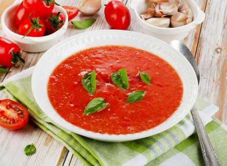 Fresh tomato soup in a white bowl on a wooden tableの写真素材