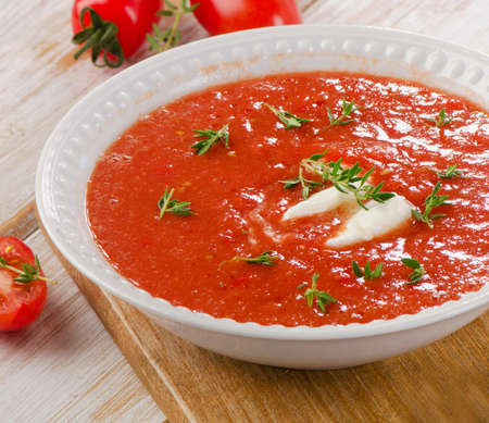 Fresh tomato soup in a white bowl on a wooden tableの写真素材