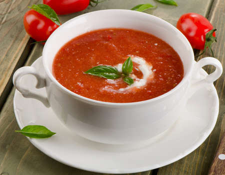 Fresh tomato soup in a white bowl on a wooden tableの写真素材