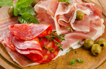 Slices of cured ham and  chorizo on a wooden table . Selective focusの写真素材