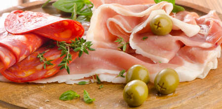 Slices of cured ham and  chorizo on a wooden table . Selective focusの写真素材
