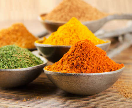colourful dried ground spices on spoons on a wooden backgroundの写真素材