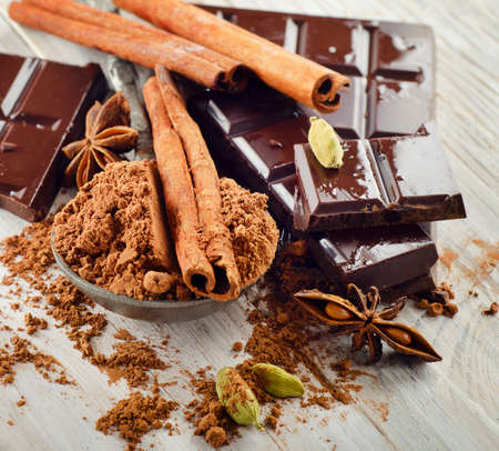 Broken chocolate bar and cocoa powder on a wooden board. Selective focus