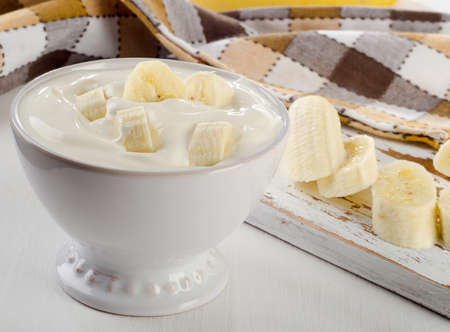 Yogurt with banana  in  white bowl   on white wooden table.の写真素材