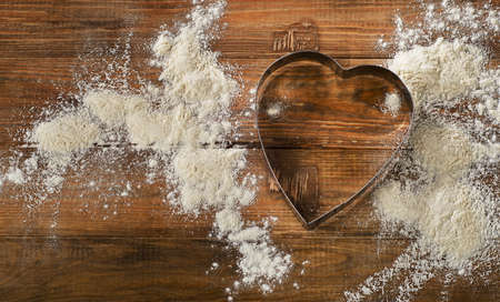 Flour and Heart-shaped cookie cutter on a worn wooden  desk.の写真素材