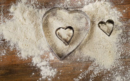 Flour and Heart-shaped cookie cutters on  worn wooden  desk.の写真素材