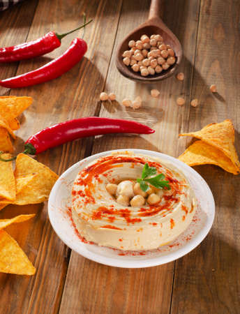 Hummus with nachos and chilli peppers on  wooden table. Top viewの写真素材
