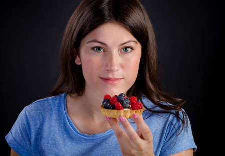 Young smiling woman eating sweet tart with fresh berries.の写真素材