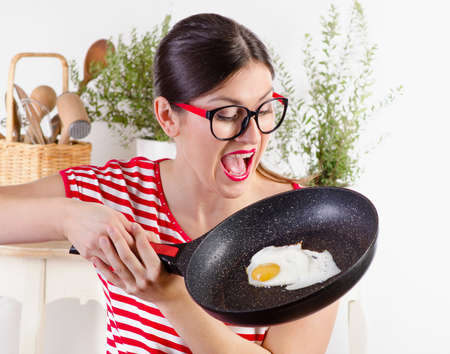 Portrait of a young happy funny woman holding frying pan with egg.の写真素材