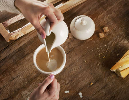 Woman pouring milk to cup of espresso coffee. Top viewの写真素材