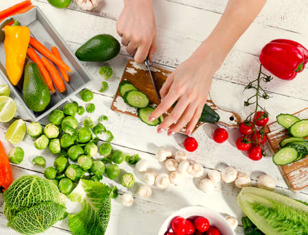 Woman hands cutting cucumber on wooden cutting board. Top viewの写真素材