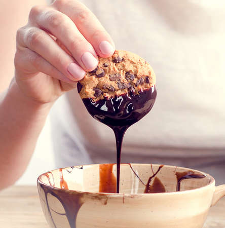 Womans hand dipping cookie in  melted chocolate.