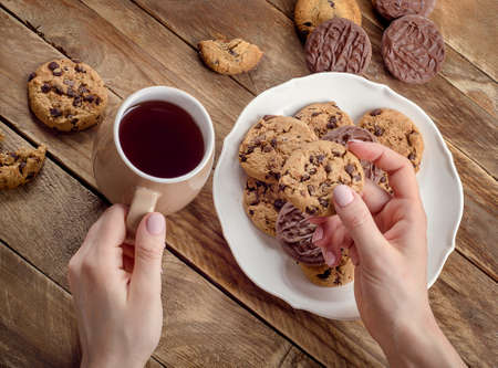 Woman hands with tea cup and chocolate cookies on  rustic wooden table. Flat layの写真素材