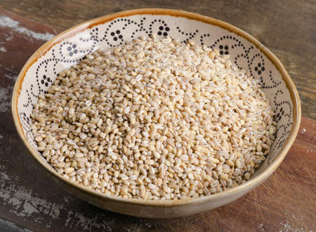 Barley in a ceramic bowl on a wooden board. Selective focusの写真素材