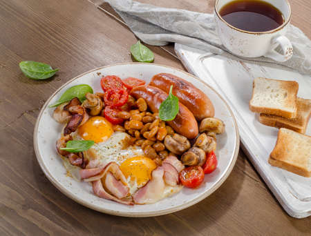 Full english breakfast with fried egg, beans, tomatoes, mushrooms, bacon, sausage and toastsの写真素材