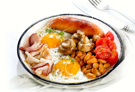 English breakfast with  fried egg, beans, tomatoes, mushrooms, bacon and sausage on a white plateの写真素材