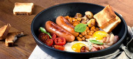 Full English breakfast with fried eggs, sausages, bacon, beans, toasts, tomatoes  and mushrooms.