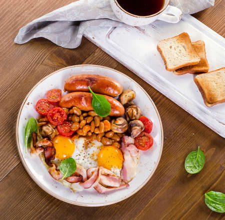Full english breakfast with fried egg, beans, tomatoes, mushrooms, bacon, sausages, toasts on wooden...