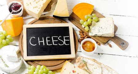 Cheese served with grapes, jam,  bread and nuts on a wooden board.