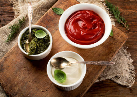 Different sauces in bowls on rustic wooden board. Ketchup, pesto, mayonnaise.