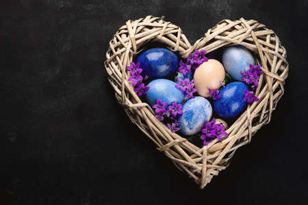 Easter eggs in heart shaped nest on black background. Top view with copy space.
