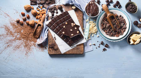 Dark bitter chocolate bars, cacao butter, cacao powder and cocoa beans on blue background. Chocolate background. Top view with copy space の写真素材