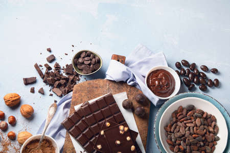 Dark bitter chocolate bars, cacao butter, cacao powder and cocoa beans on blue background. Chocolate background. Top view with copy space の写真素材