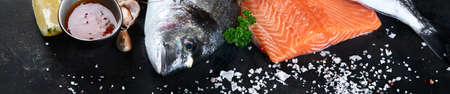 Fresh raw fish and seafood on black background. Panorama, banner