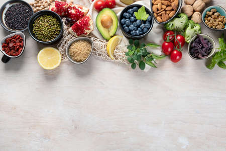 Healthy food selection on white wooden background. Fresh fruits, superfoods an vegatables. High in antioxidants, vitamins, minerals, fiber. Top view with copy space.の写真素材