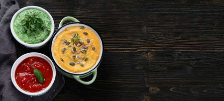 Vegetables cream soups on dark wooden background. Top view with copy space. Panorama banner