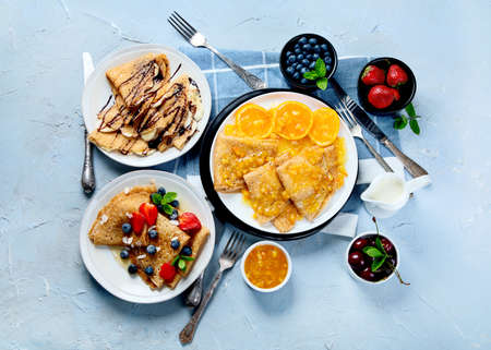 Variety of fresh crepes with jam, fruits and berries on gray background. Homemade delicious crepes....