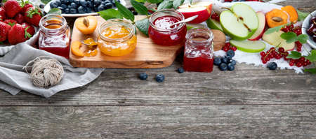 Assortment of homemade jams in glass jars and seasonal berries, fruits on rustic wooden background....