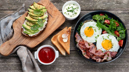 Traditional breakfast with Fried Eggs in pan and vegan avocado sandwich on a wooden background. Top viewの写真素材