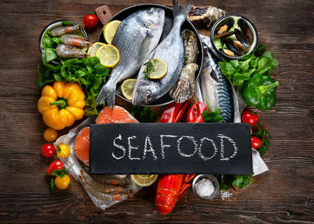 Fresh fish and seafood with herbs, spices and vegetables on rustic wooden background. Balanced diet and cooking concept. Healthy eating. Top view, flat layの写真素材