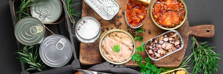 Various canned fish and seafood in aluminum cans. On dark gray background. Top view, panoramaの写真素材