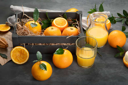 Oranges with leaves in wooden box, orange juice on dark gray backgroundの写真素材