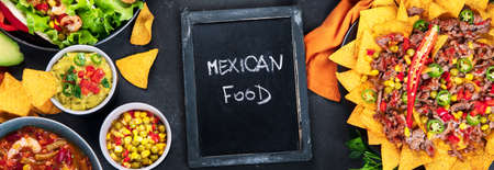 Delicious hispanic mexican meal board with nachos, tacos, guacamole, shrimps, avocado and starfruit. Hot and spicy. Top view, panorama bannerの写真素材