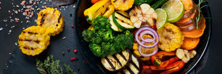 Grilled assorted vegetables in cast iron pan on black background. Grill menu. Top view, panorama