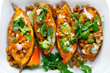 Stuffed sweet potato with spiced chickpea, dressing and herbs. Homemade vegan food concept. Top viewの写真素材