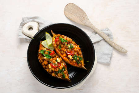 Stuffed sweet potato with spiced chickpea, dressing and herbs. Homemade vegan food concept. Top view, copy spaceの写真素材