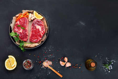 Meat raw steaks with seasoning and herbs on dark background. Healthy food concept. Top view, copy spaceの写真素材