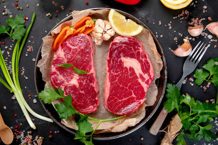 Meat raw steaks with seasoning and herbs on dark background. Healthy food concept. Top view