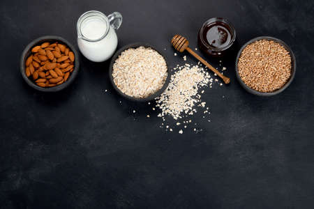 Rolled oat flakes in black bowls and golden wheat ears on dark background. Top view, copy spaceの写真素材