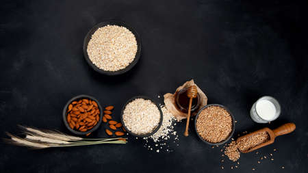Rolled oat flakes in black bowls and golden wheat ears on dark background. Top view, copy space