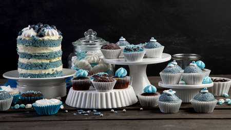 Delicious cake and cupcakes in blue on wooden background. Table setting for celebration.の写真素材