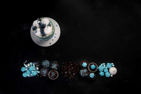 Delicious cake and cupcakes in blue on dark background. Table setting for celebration. Top view,...