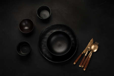 Table setting with a black plates on a black background. Minimalism concept. Top view, copy space