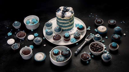 Delicious cake and cupcakes in blue on dark background. Table setting for celebration.の写真素材