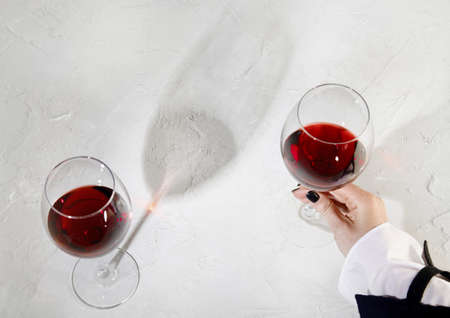 Young woman holding glass of red wine on white background. Hand with black polish.